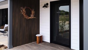 A modern building exterior with a dark wooden panel wall, a black door labeled "barrel room," and a small wooden stool on the porch. - Shawwood Estate (Bombira)