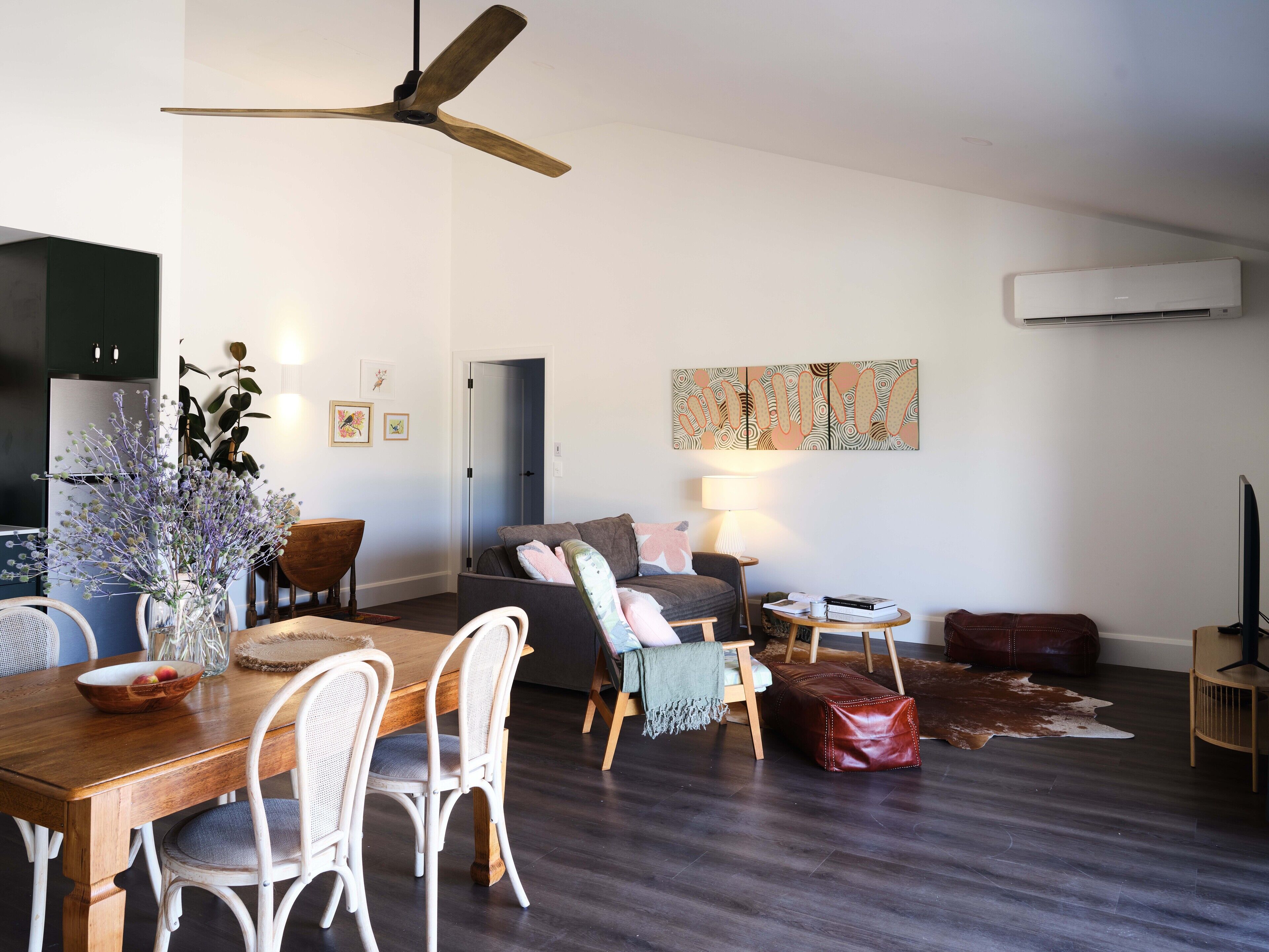 A modern living room with a dining area, a ceiling fan, a flat-screen TV, and an air conditioning unit.