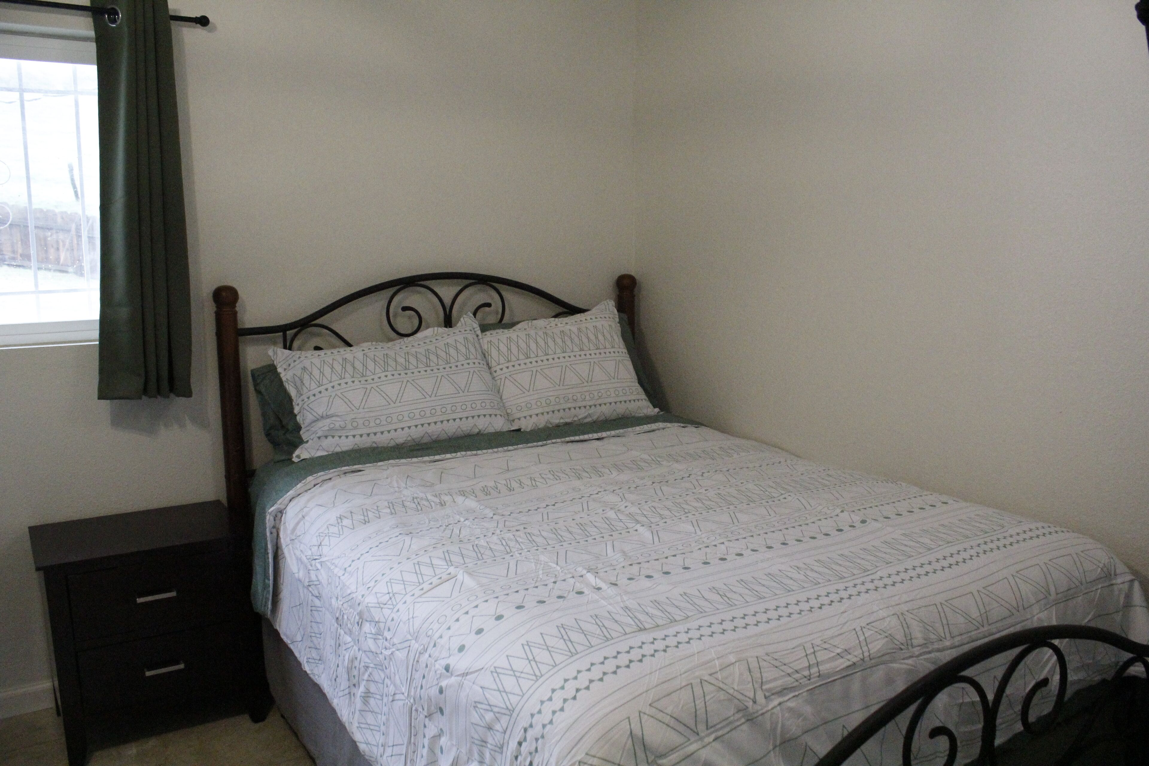 Un lit avec une couvre-lit à motifs, une table de chevet avec des tiroirs et une fenêtre avec un rideau.