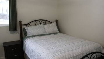 Un lit avec une couvre-lit à motifs, une table de chevet avec des tiroirs et une fenêtre avec un rideau.