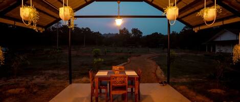 Un área de comedor al aire libre con una mesa y sillas, rodeada de macetas colgantes y vistas a un paisaje rural.