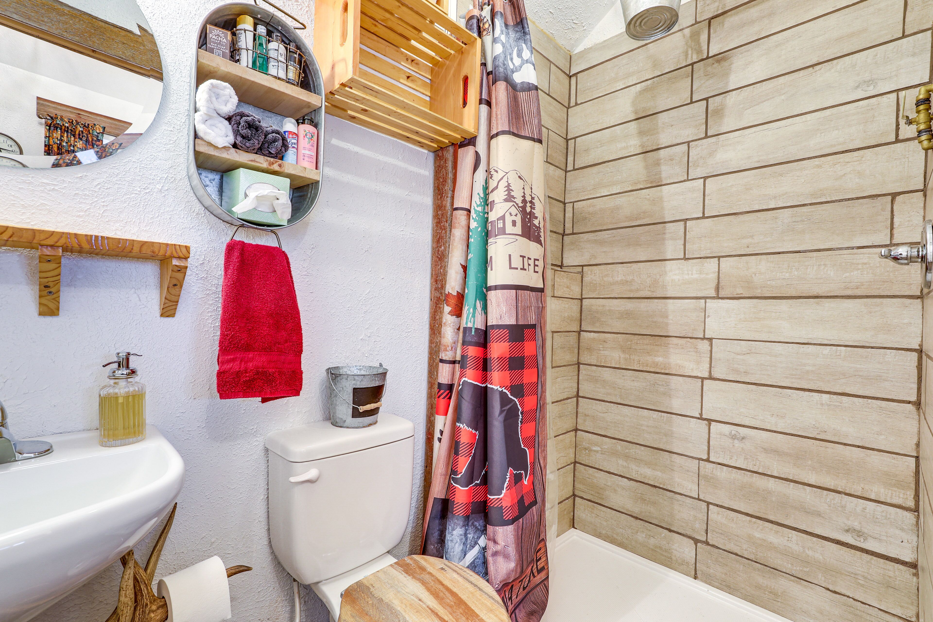 Un baño con tocador de madera, lavamanos, inodoro y cortina de ducha con motivos de vida.