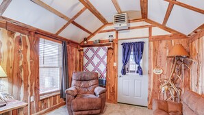 L’intérieur chaleureux d’un chalet avec des murs en bois, un fauteuil en cuir, un canapé, une courtepointe et une porte ornée de bois de cerf décoratif.