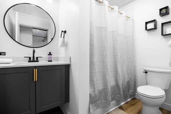 Een moderne badkamer met een witte wastafel, een zwarte kraan en een ronde spiegel.
