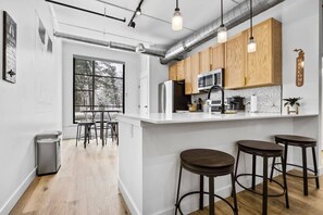 A modern kitchen with white cabinetry, stainless steel appliances, and a bar area with stools. - Rooftop Hot Tubs I Dogs Welcome I Near DT TC (Traverse City)