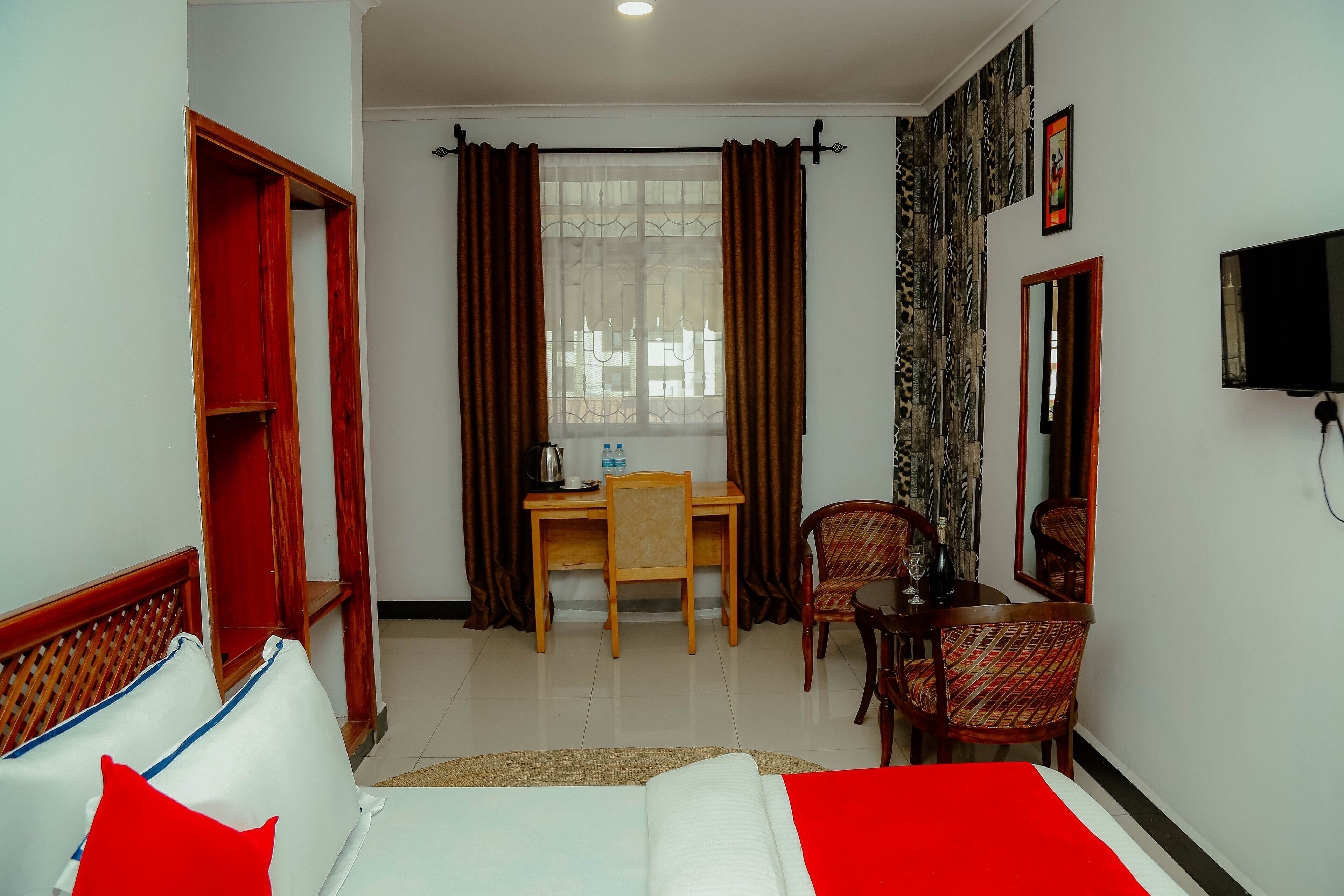A hotel room with a bed, a desk, two chairs, a TV, and a window with curtains.