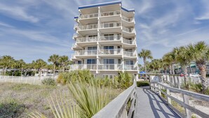 A multi-story hotel with balconies, a wooden boardwalk, and palm trees. - Sunny Fort Walton Beach Condo - Walk to Ocean! (Fort Walton Beach)