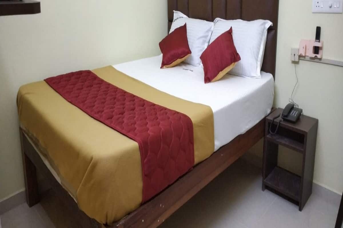 A bed with a brown headboard, white and red pillows, and a beige and red bedspread.