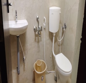 A bathroom with a white sink, a toilet, and a wall-mounted bidet. - Yoga Inn (Puducherry)