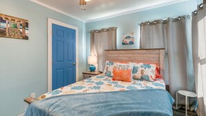 A bedroom with a blue door, a bed with a beach-themed bedspread, a nightstand with a lamp, and a ceiling fan. - 2 Mi to Redfish Bay: Aransas Pass Home w/ Fire Pit (Aransas Pass)