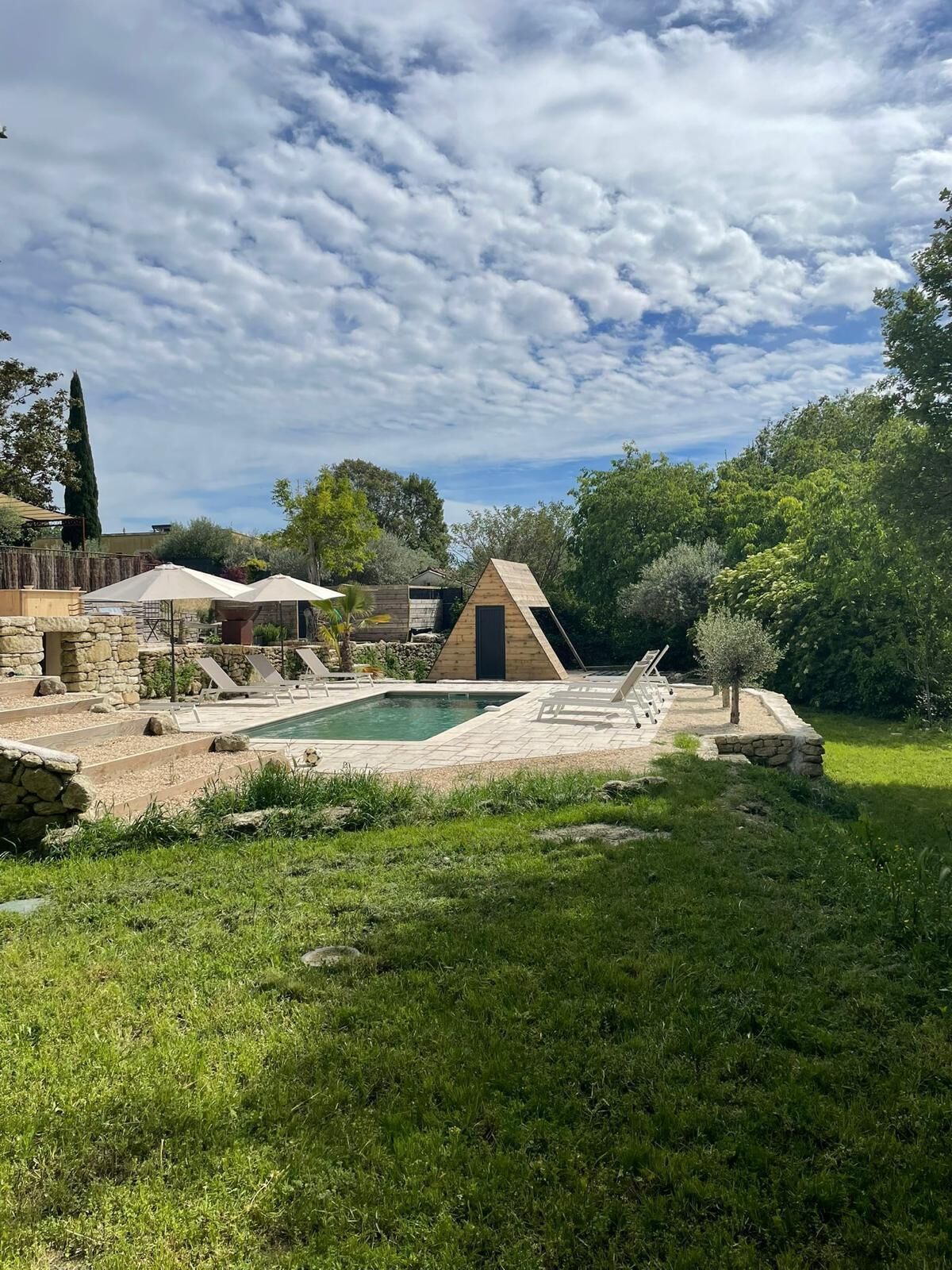 A backyard with a swimming pool, lounge chairs, and a small wooden structure.