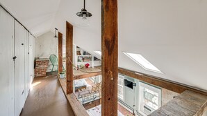 Ett rum i loftstil med synliga träbjälkar, ett takfönster och utsikt över det intilliggande rummet.