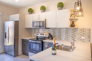 A modern kitchen with stainless steel appliances, a microwave, a stove, and a sink. There are potted plants on the cabinets and a bottle of wine on the counter. - Stunning Condo in Luxe Resort Azzurro by Bocobay (Noord)