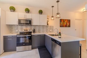 A modern kitchen with a built-in oven, microwave, and dishwasher, a large island with a sink, and potted plants on the cabinets.