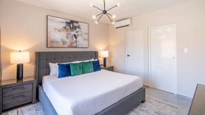 Un dormitorio moderno con una cama grande, dos mesitas de noche con lámparas, un aplique de techo y un cuadro abstracto de gran tamaño en la pared.