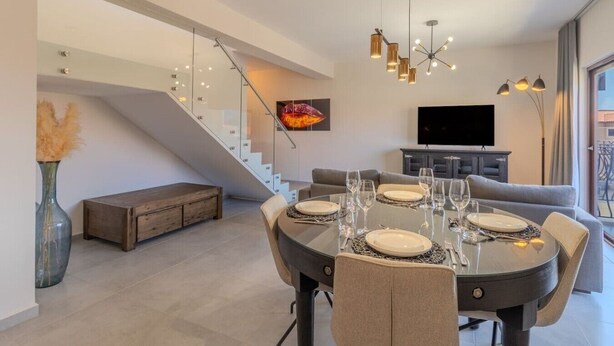 Una sala de estar moderna con una mesa de comedor preparada para cuatro personas, una escalera, un televisor de pantalla plana y un sofá.