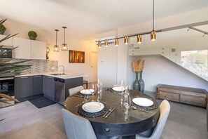 A modern kitchen with a central island, dining table set for four, and pendant lighting.