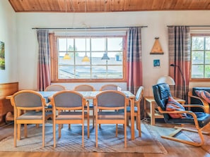 Ein Essbereich mit Holztisch und Stühlen, einer Couch und Blick durch große Fenster ins Freie.