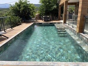 Ein klares Schwimmbecken mit Holzterrasse und Liegestühlen.