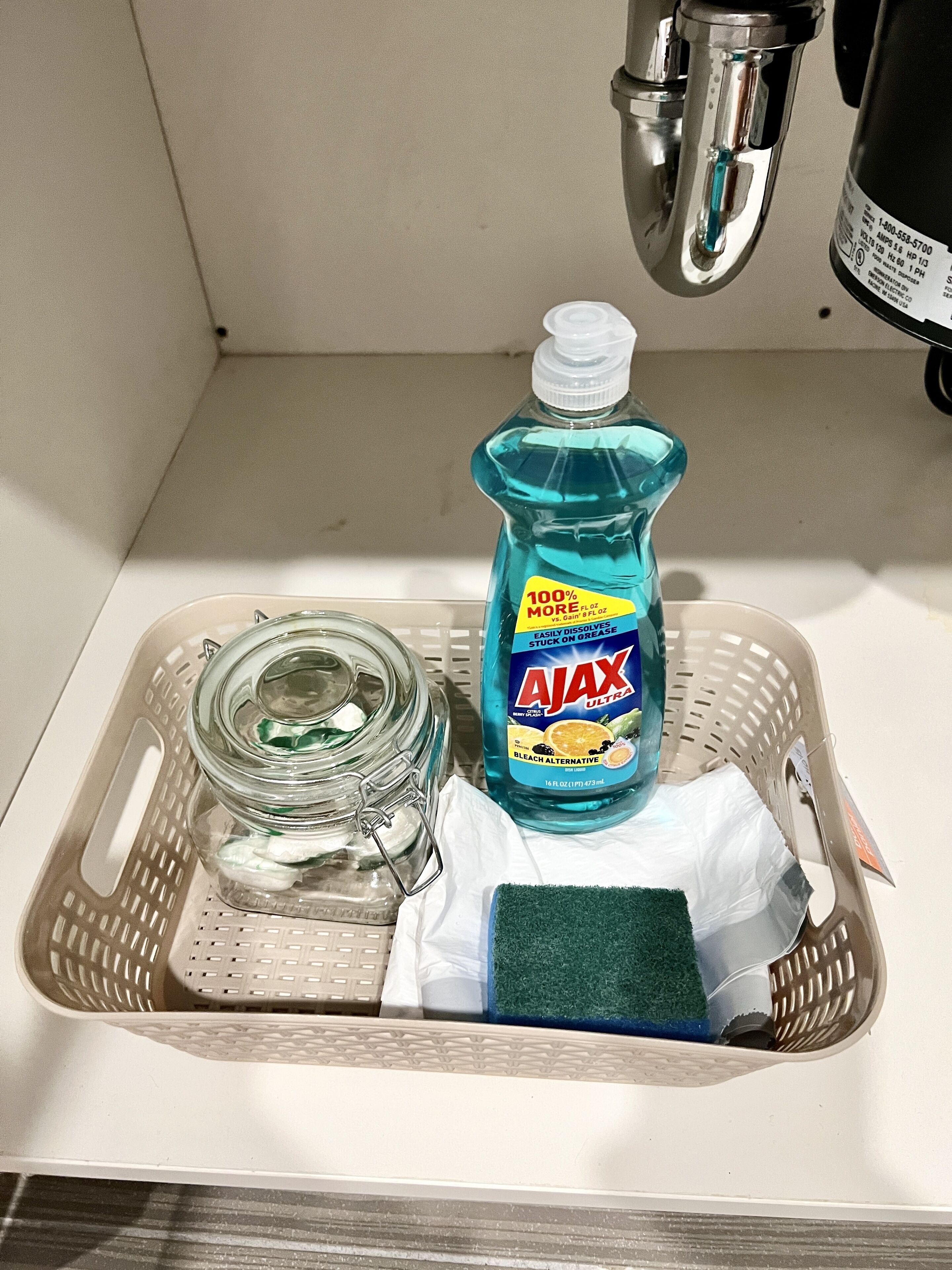 A bathroom sink with a bottle of Ajax Ultra dish soap, a glass jar, a sponge, and a white cloth.