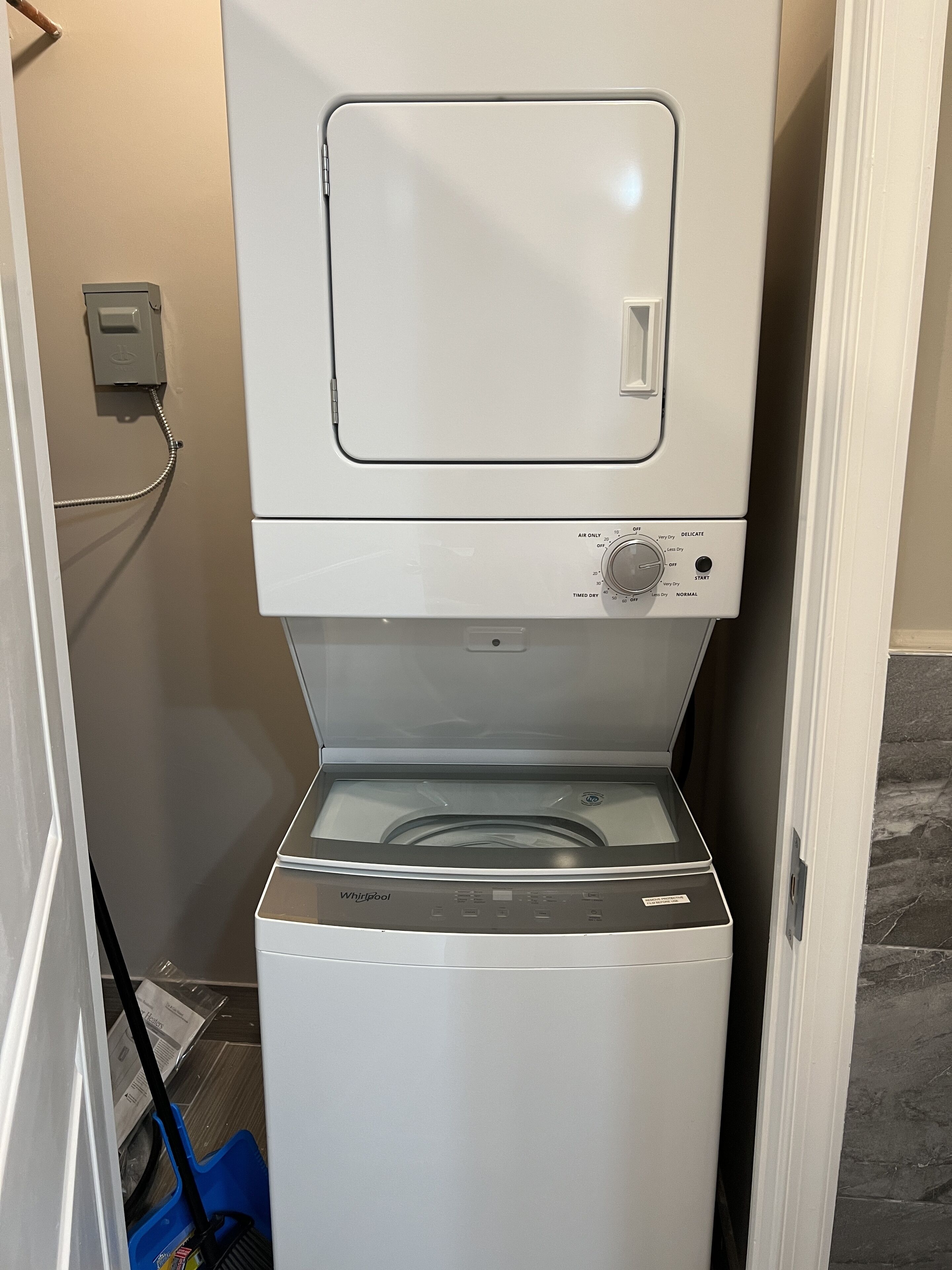 Een voorlader wasmachine en droger van Whirlpool in een wasruimte, met een mop en emmer in de buurt.