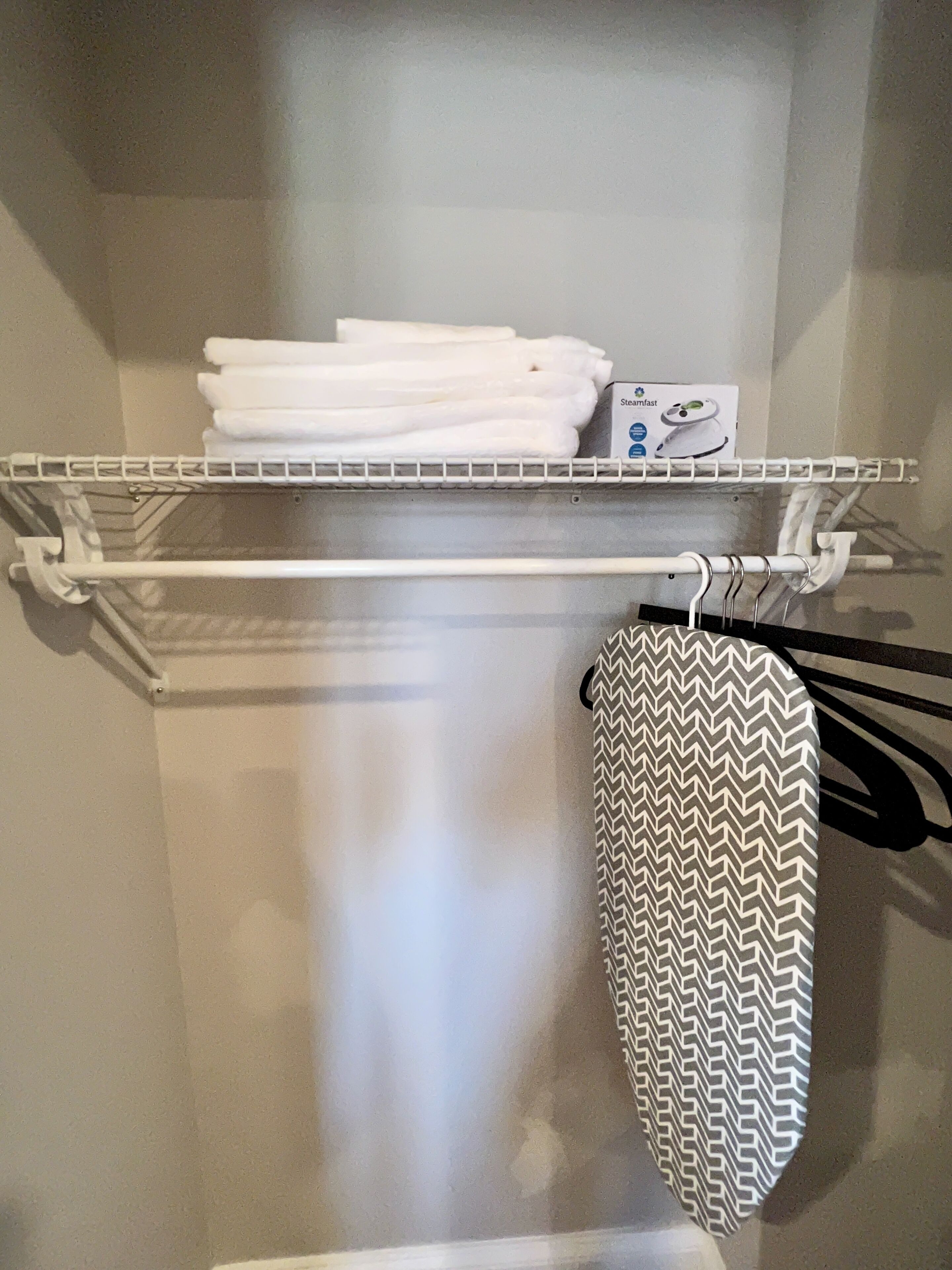 Une salle de bain avec un porte-serviettes sur lequel sont pliées des serviettes et un fer à repasser à vapeur accroché au mur.