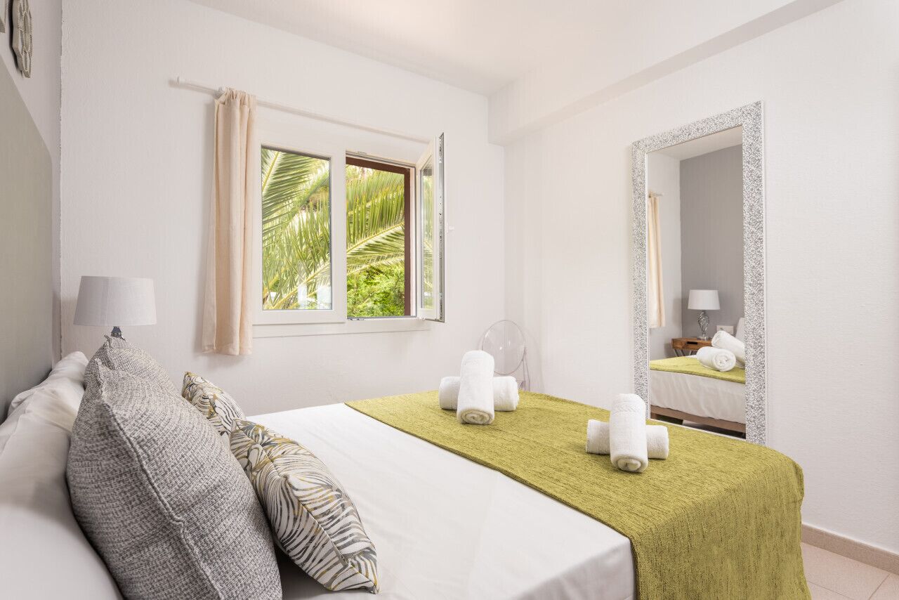 A hotel room with a bed, a window with curtains, a mirror, and a view of palm trees.