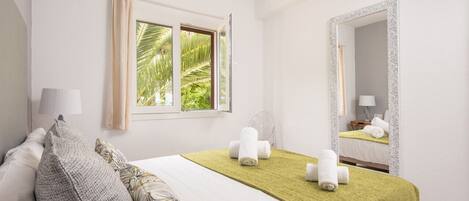 A hotel room with a bed, a window with curtains, a mirror, and a view of palm trees.