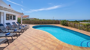 A swimming pool with lounge chairs, a tiled deck, and a view of the sea.