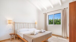 A bedroom with a bed, bedside lamps, a window with curtains, and a small stool.