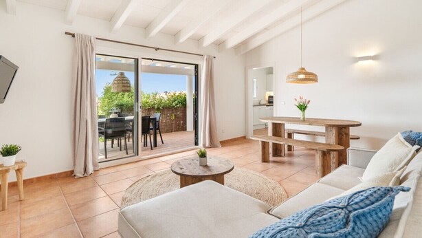 A modern living room with a sofa, a round coffee table, and a wooden dining table. There is a sliding glass door leading to an outdoor area with a patio table and chairs. - Menorca Sur T3, 3 bedroom (Torre Soli Nou)