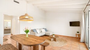 A spacious living area with a wooden dining table, a sofa, and a television mounted on the wall. - Menorca Sur T3, 3 bedroom (Torre Soli Nou)