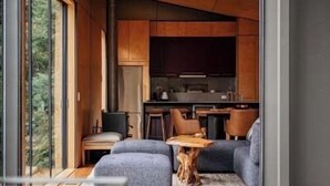 A modern interior with a cozy seating area, a kitchen with dark cabinets, and a large window offering a view of the outdoors. - Hidden on Huon, exclusive getaway (Police Point)