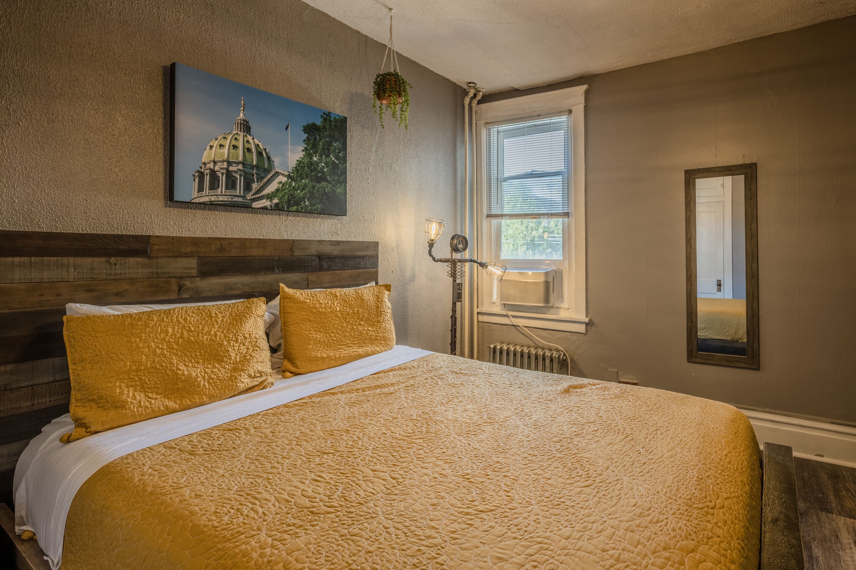 Une chambre à coucher avec un grand lit, un tableau représentant un bâtiment accroché au mur, une fenêtre avec des stores et un radiateur.