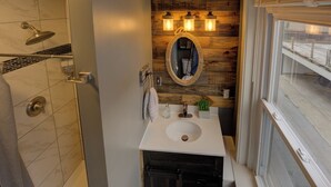 A bathroom with a shower, a sink with a mirror, and a wooden wall.