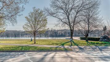 Un parc avec un sentier dallé, des arbres et une étendue d’eau en arrière-plan.