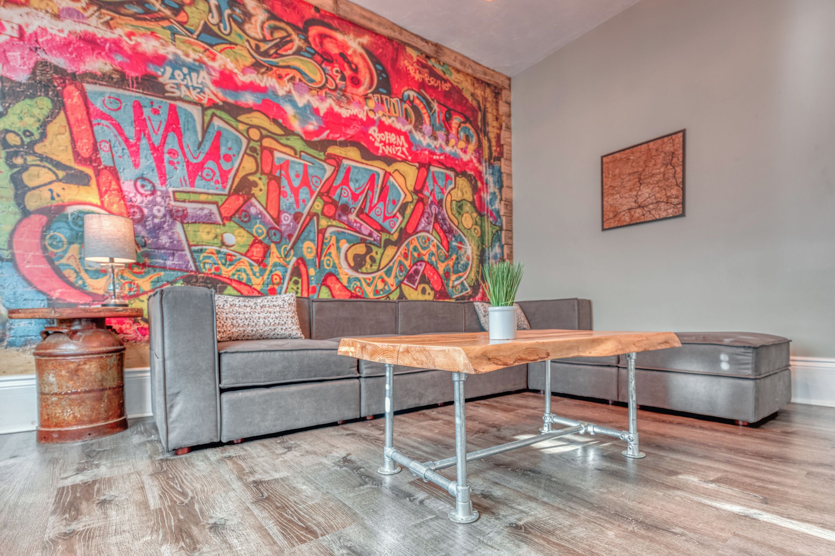 A modern living room with a grey sofa, a wooden coffee table, a colorful graffiti wall, and a small potted plant.