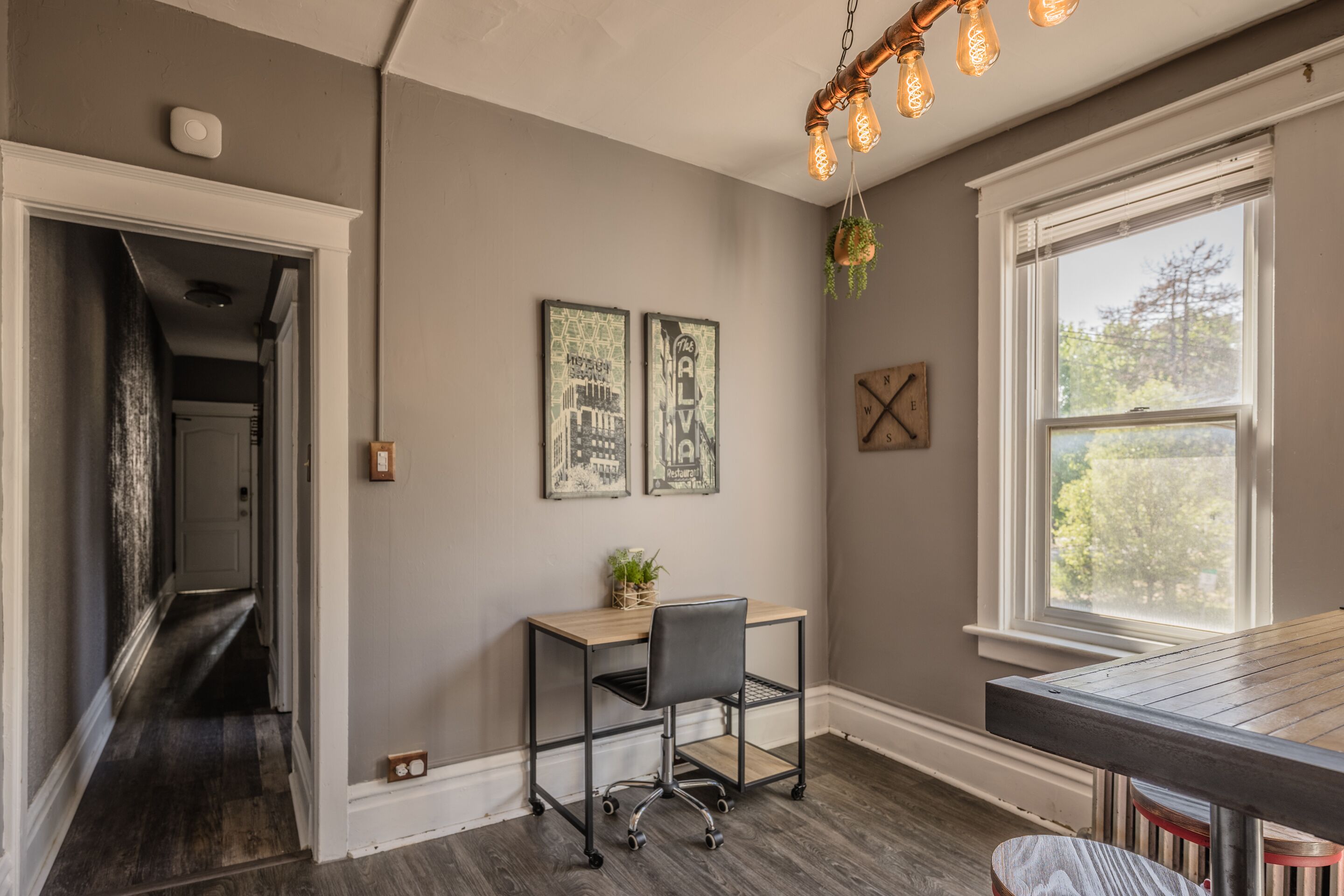 Una habitación con escritorio, silla y ventana que da a árboles.