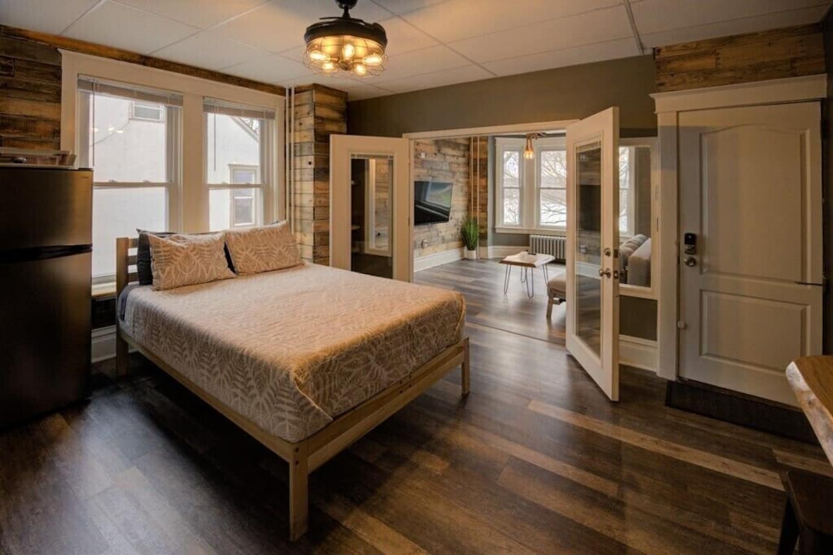 A spacious bedroom with a large bed, wooden flooring, and a modern ceiling light.