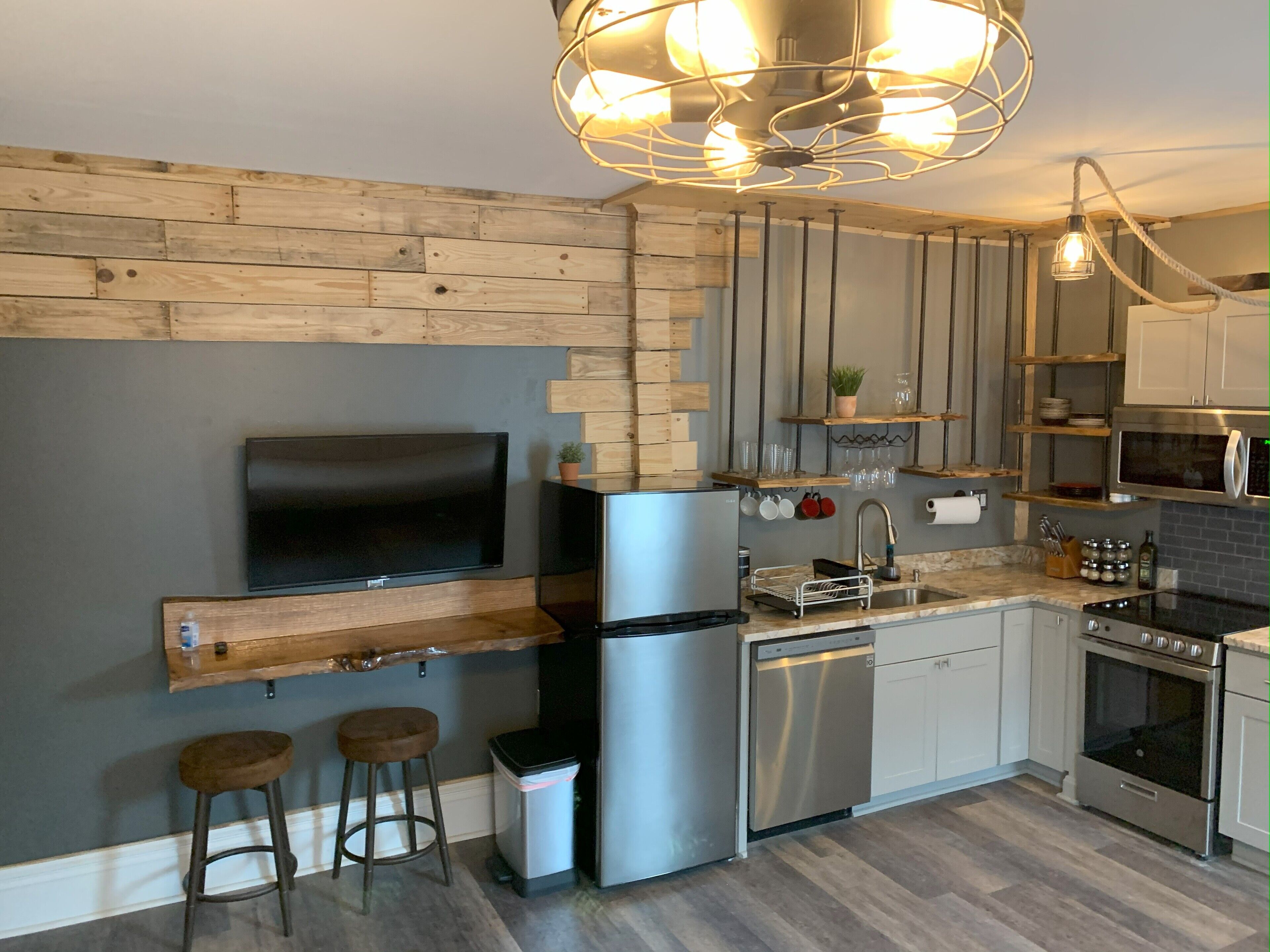 A modern kitchen with a built-in TV, stainless steel appliances, wooden accents, and a hanging light fixture.