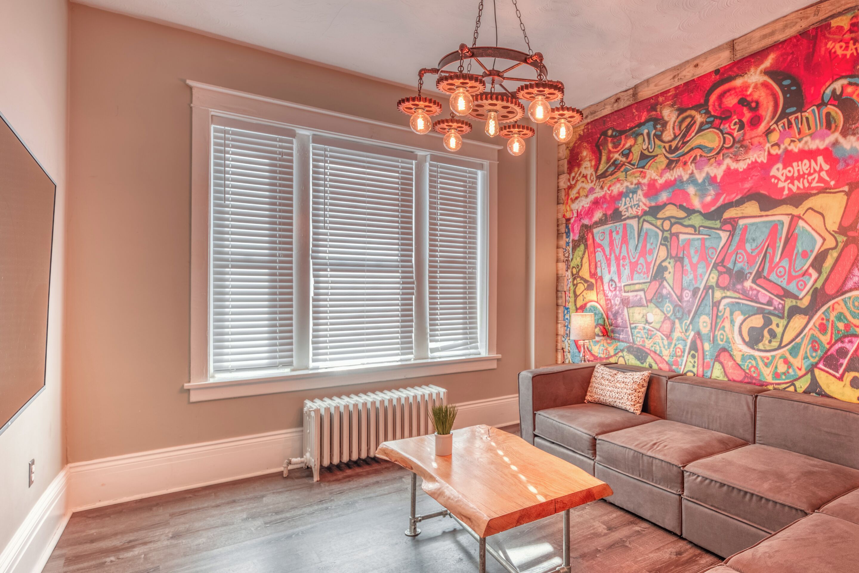 Una sala de estar con un ventanal grande, un sofá, una mesa de centro y una pared con grafitis coloridos.