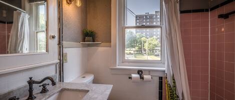 A bathroom with a white sink, a toilet, a window, and a shower curtain.
