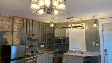 A modern kitchen with stainless steel appliances, wooden accents, and a unique pendant light fixture.
