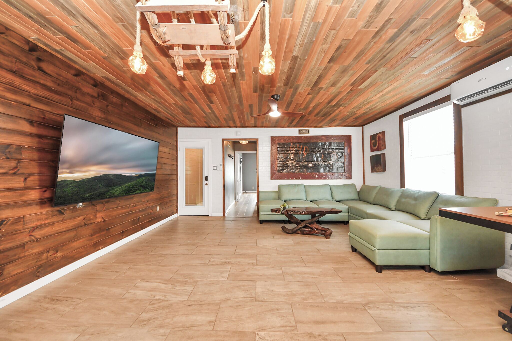 A modern living room with a wooden ceiling, a flat-screen TV, a green sofa, and a wooden coffee table.