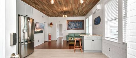 A modern kitchen with a wooden ceiling, stainless steel appliances, and a green sofa.