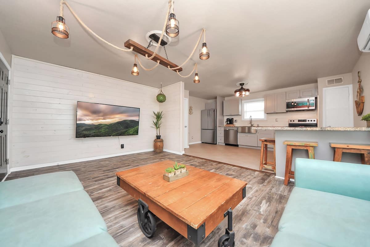 A spacious living area with a wooden coffee table, light blue sofas, and a large flat-screen TV mounted on a white wall.