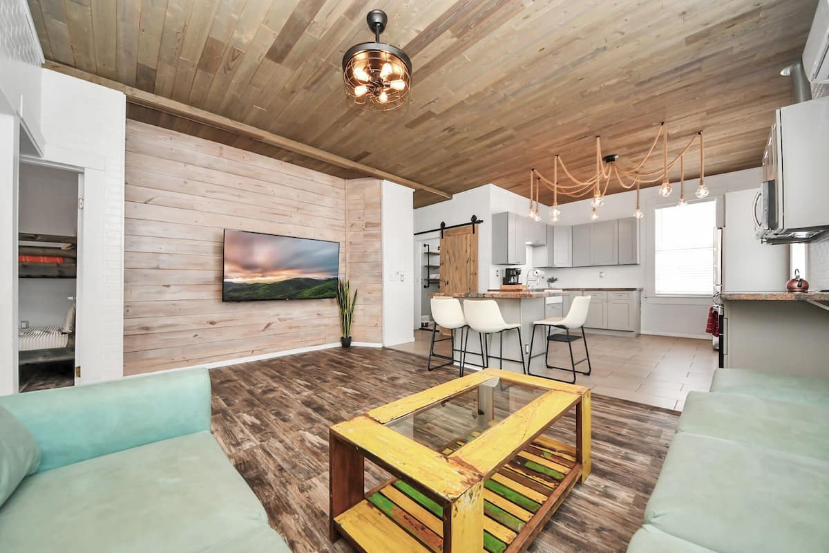 A modern living room with a wooden ceiling, a glass coffee table, and a painting on the wall.