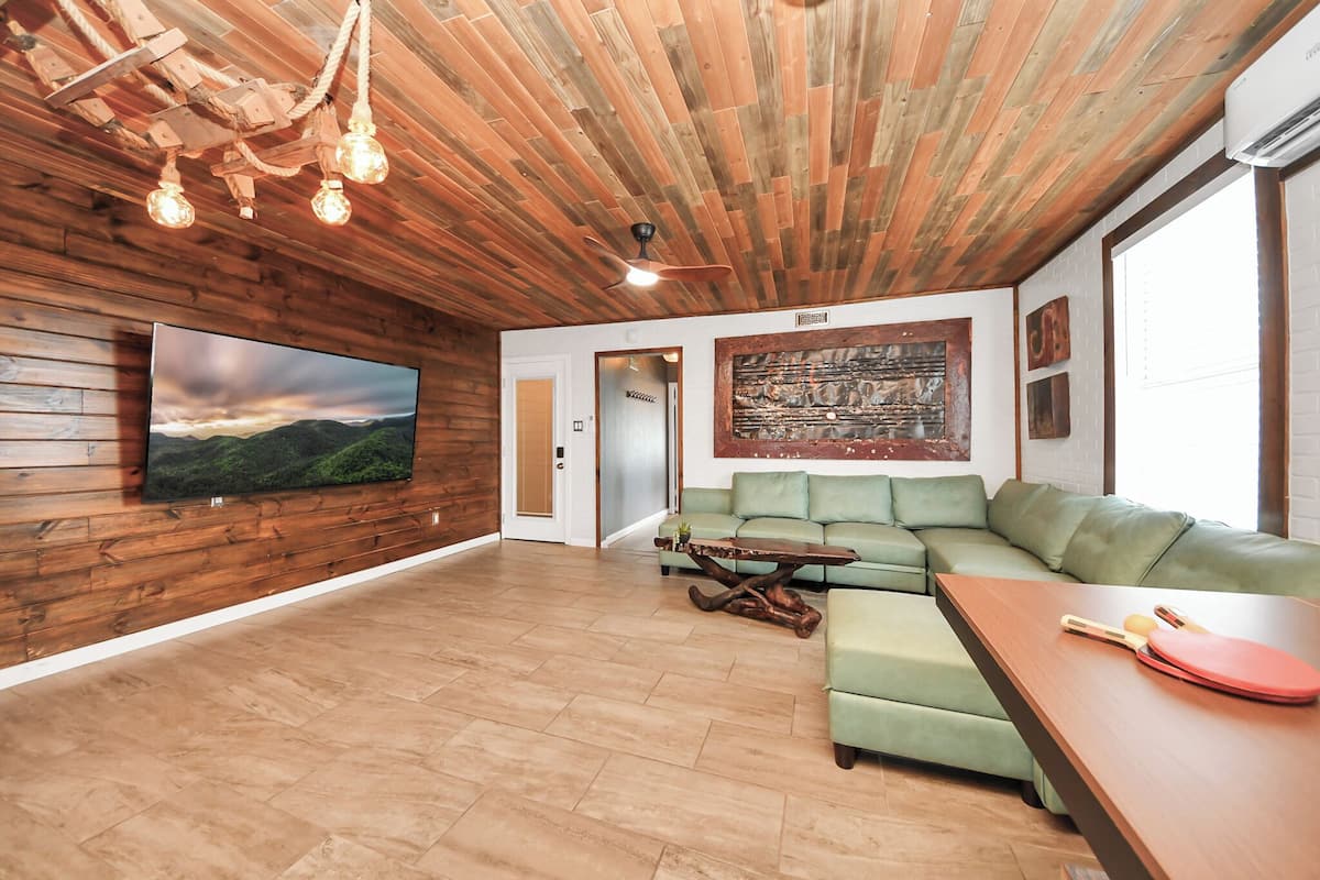 A modern living room with a wooden ceiling, a green sofa, a wooden coffee table, and a flat-screen TV mounted on the wall.