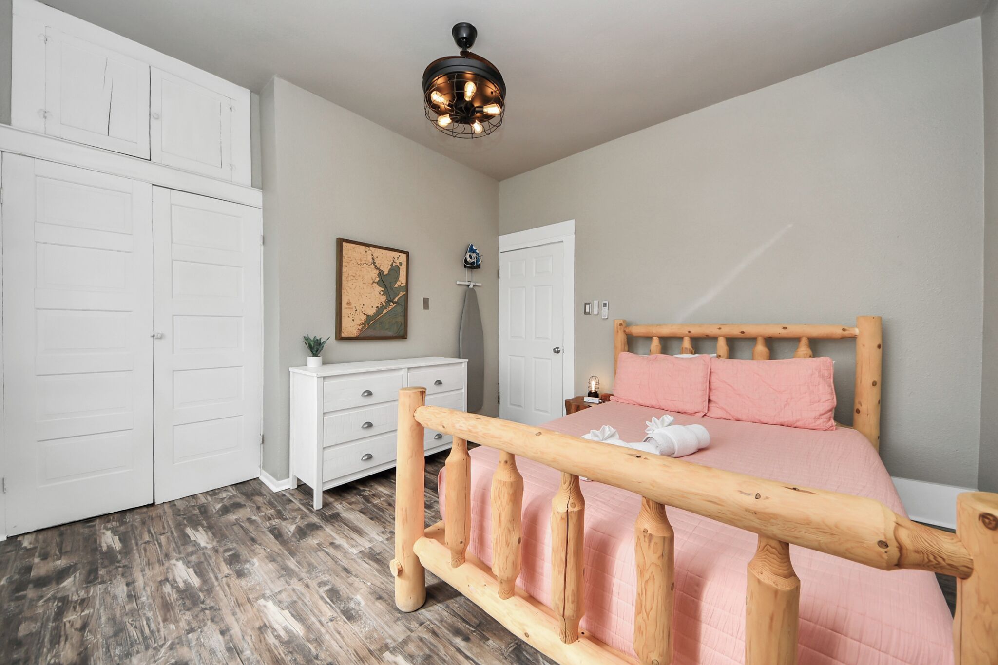 A bedroom with a wooden bed frame, a white dresser, a white wardrobe, and a ceiling fan.