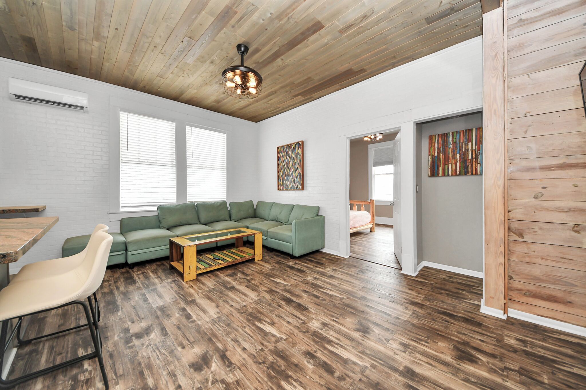 Un salon spacieux avec un canapé d’angle vert, un plancher en bois et un ventilateur de plafond.